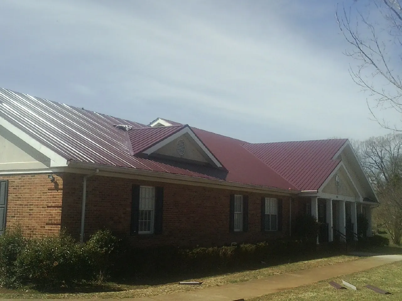 Red metal roof with gabled entries on a long brick building, from a Hail Damage Roof Repair job in Goodrich