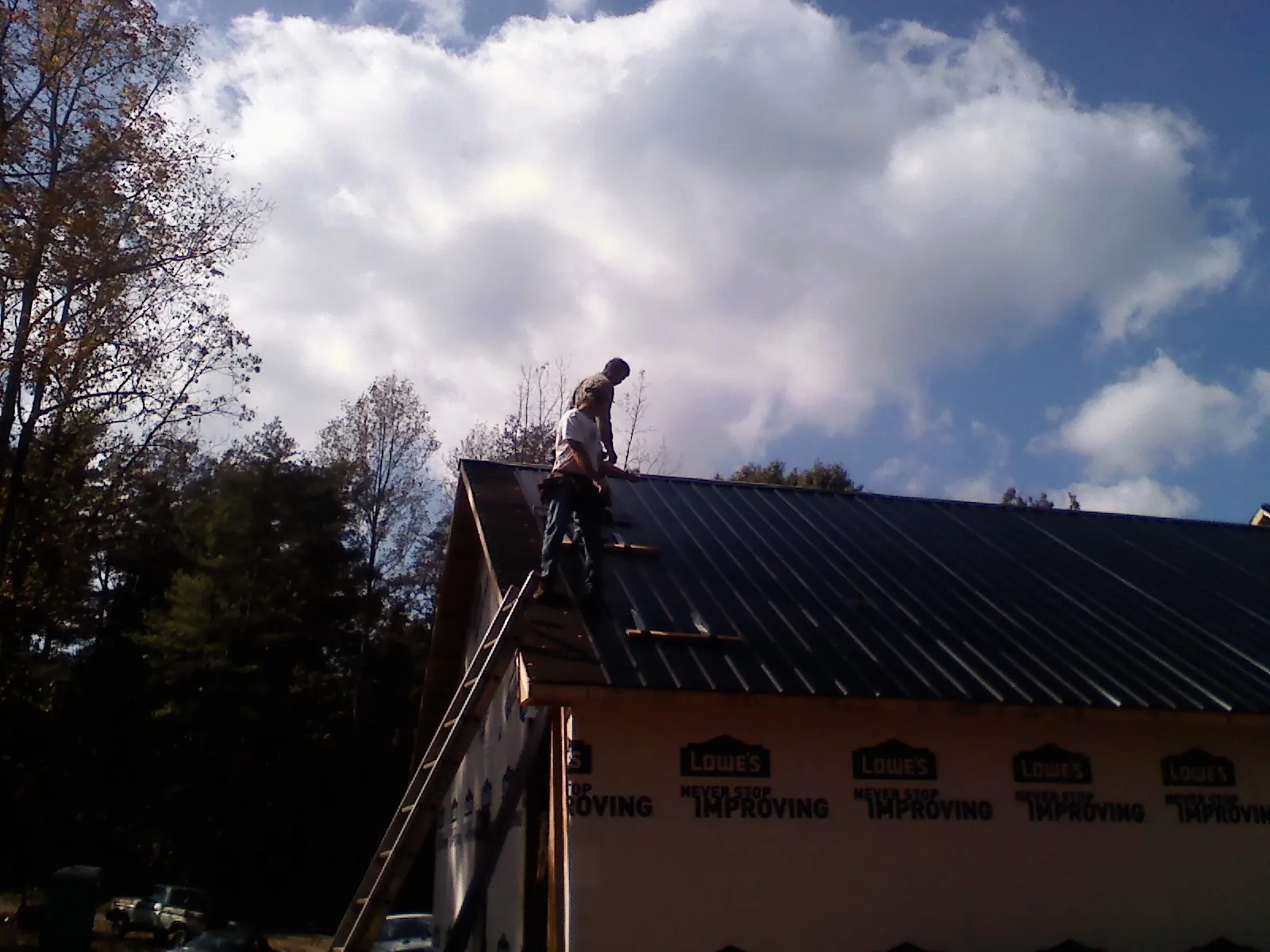 Roofer fastening dark metal panels high against a cloudy sky, from a Roof Inspection job in Goodrich