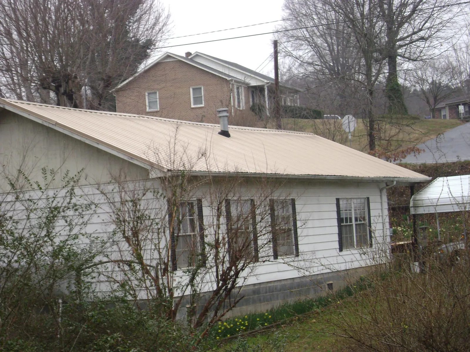 Tan metal roof on a white sided house set into a hillside — Commercial Roofing by Roofing Brothers in Goodrich
