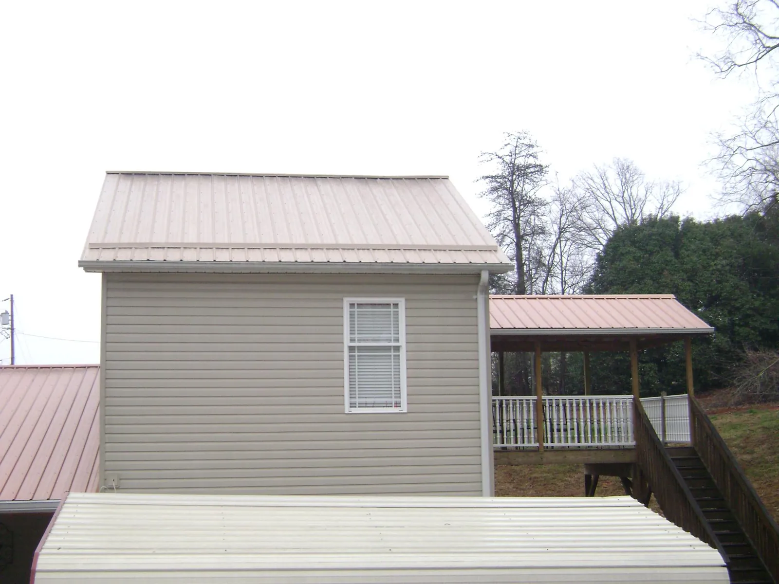 Tan metal roofs on a two story addition and attached porch, from a Roof Replacement job in Goodrich